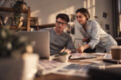 Man en vrouw bekijken samen kleurstalen en ontwerpen op een laptop aan een bureau.